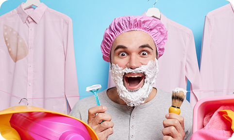 Man wearing shower cap with shaving foam on his face, smiling with a razor in hand